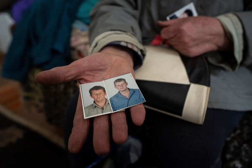 A weathered hand holds out two small photos of a young to middle-aged man.