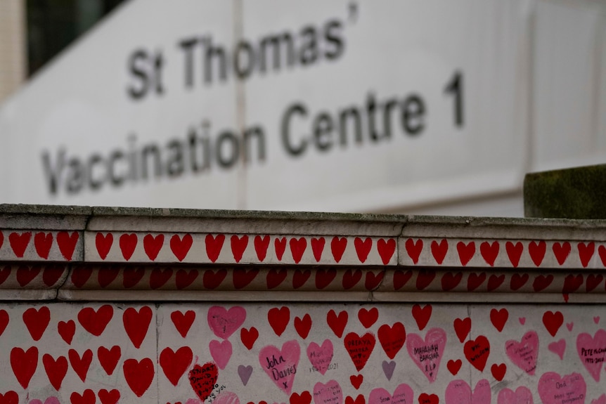 A vaccination centre sign is visible behind a wall covered in hearts