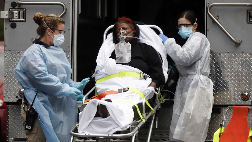 Emergency Medical Technicians  wearing protective gears wheel a sick patient to a waiting ambulance.