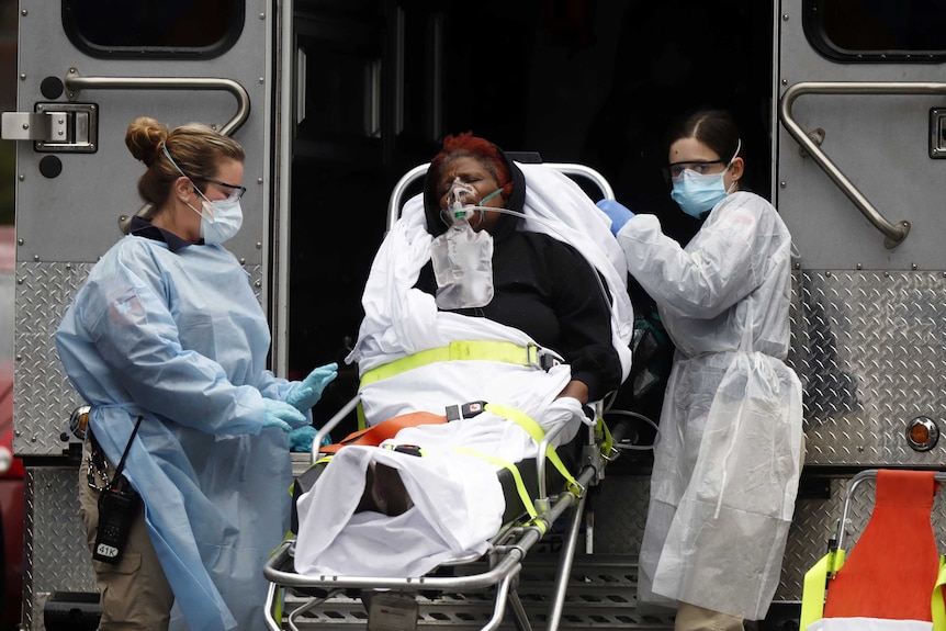 Emergency Medical Technicians  wearing protective gears wheel a sick patient to a waiting ambulance.