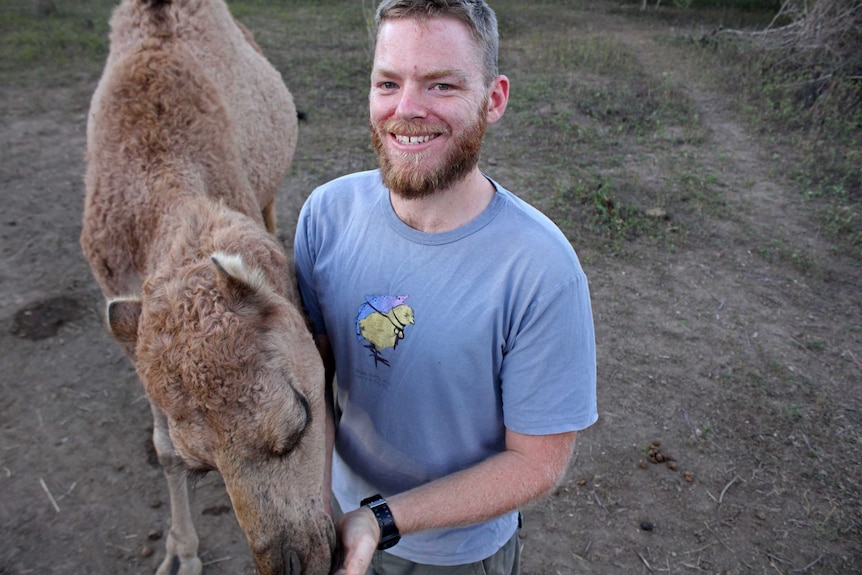A man smiles as he pats a camel