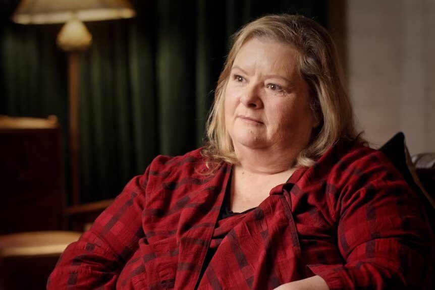 A photo of a woman wearing a dark red top, shoulder-length blonde hair.