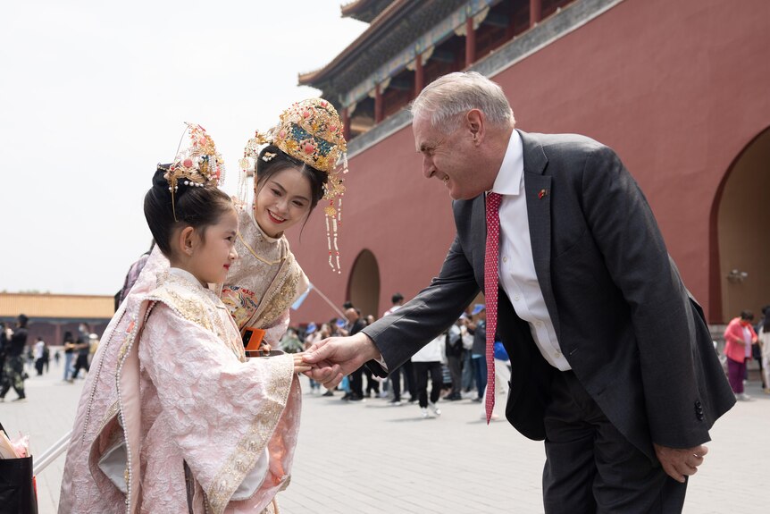 Trade Minister Don Farrell shakes hands with a child in a traditional costume in China's Forbidden City. 