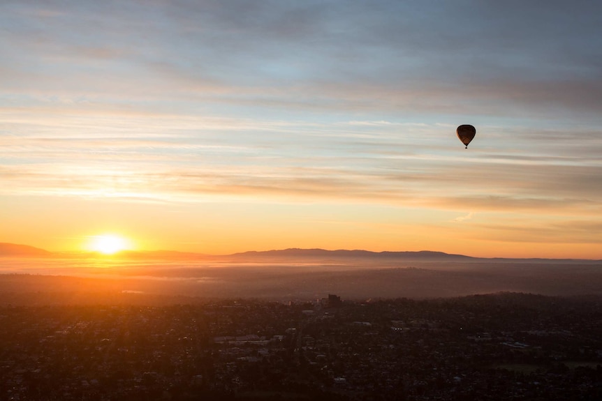 A single hot air balloon is silhouetted against a wide expanse of sky as the rising sun turns things golden.