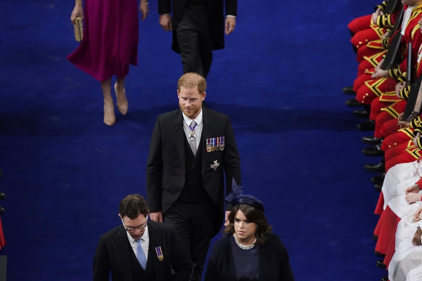 Prince Harry walking on a blue carpet, alone. 
