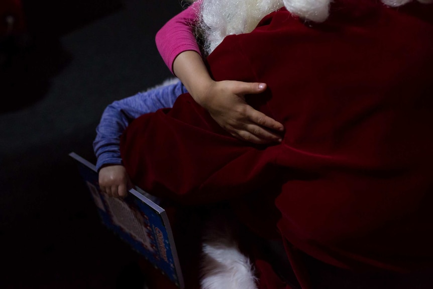 Kids arms wrap around a big red suit as children hug Santa.