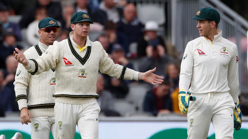 Steve Smith stands with his arms outstretched with David Warner and Tim Paine during a Test match.
