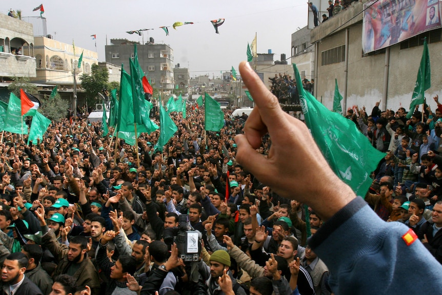 Crowd of people fill the streets, waving green Hamas flags.