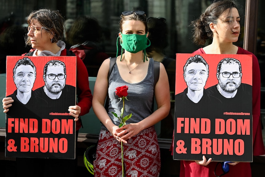 Demonstrators hold placards and roses as they protest outside the Brazilian Embassy in London