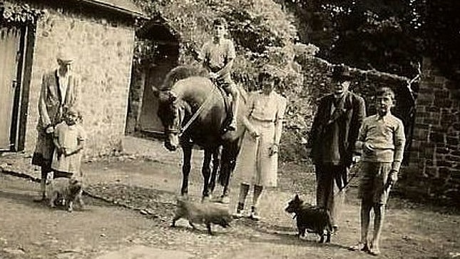A black and white photo shows john as a teenager riding a horse as family members stand by