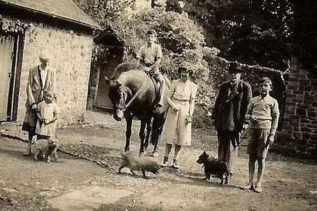 A black and white photo shows john as a teenager riding a horse as family members stand by