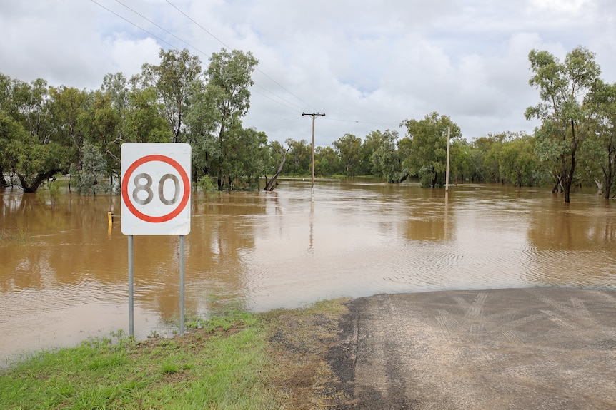 A speed sign is flooded in brown water.