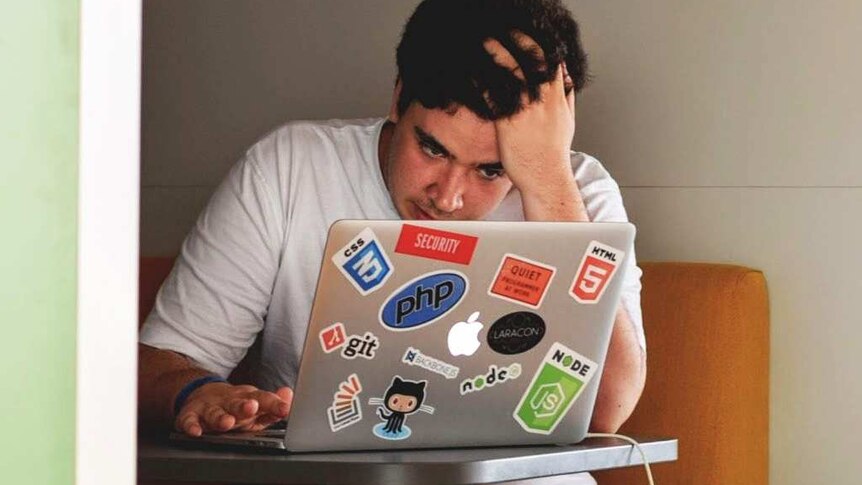 A stressed man looks at a laptop computer covered in stickers.