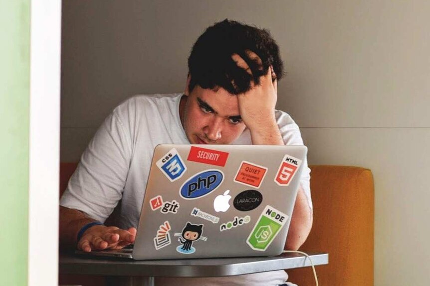 A stressed man looks at a laptop computer covered in stickers.