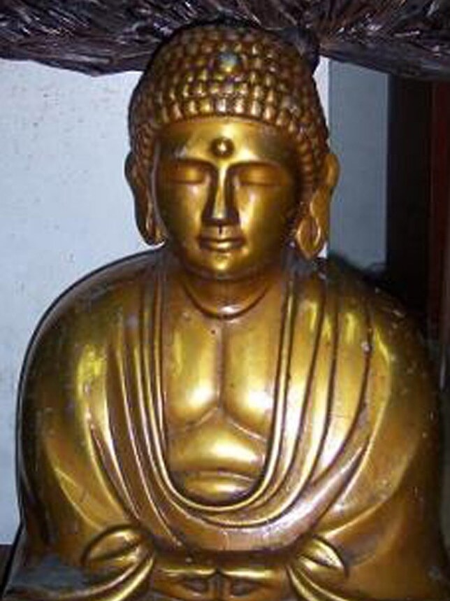 A golden statue of buddha sitting with his eyes closed and hands clasped 