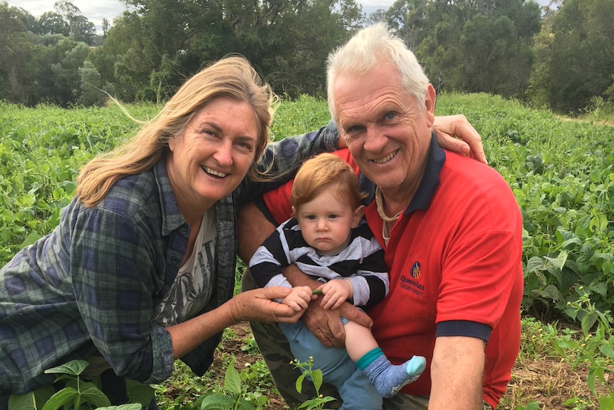 Sandi and Dave Cohen crouch in their bean field with grandson Hendrix.