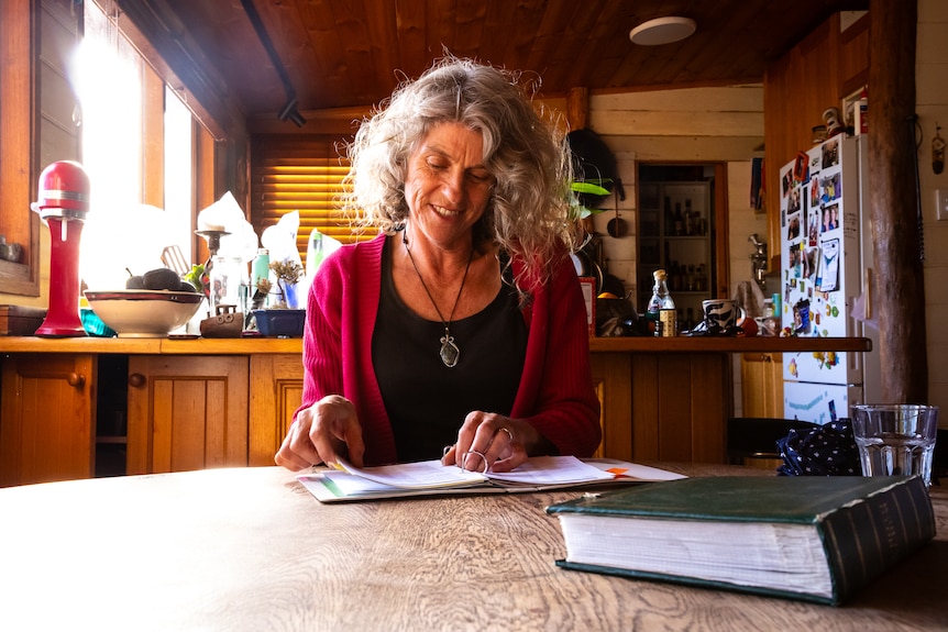 An older woman sits at her kitchen table, working on a document.