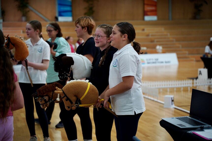 A group of young girls talk as they examine an indoor hobby horse riding course