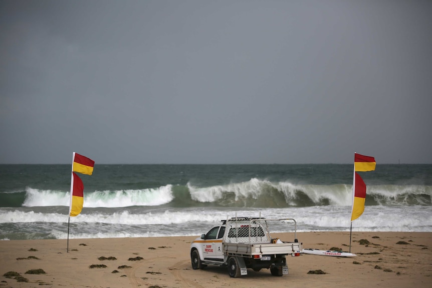 A wide shot of Trigg Beach with a surf rescue vehicle and lifesaver flags on the beach and waves crashing in a big swell.