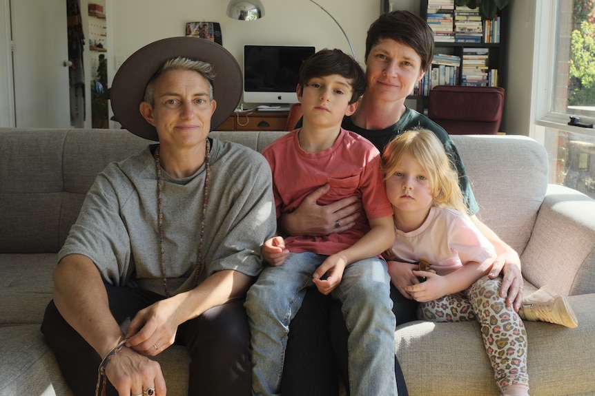 A family of two women, a young boy and a young girl pose on a couch. 