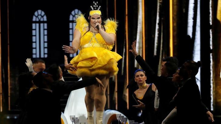 Netta walks on a table singing as dancers reach out to her from either side below. She wears a yellow dress.