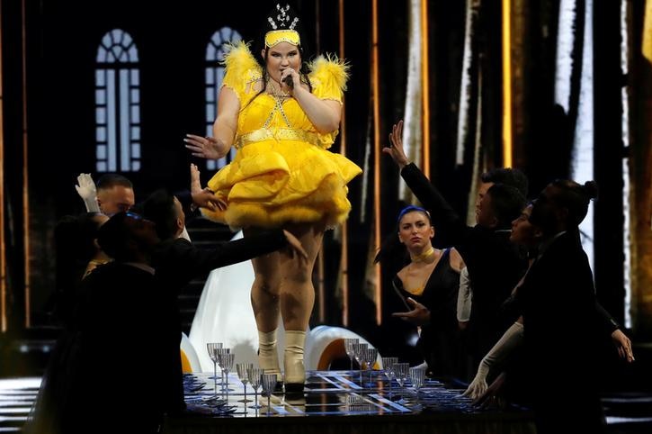 Netta walks on a table singing as dancers reach out to her from either side below. She wears a yellow dress.