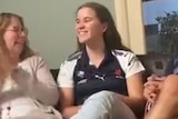 Video screenshot of Ellie McKenzie smiling widely, while flanked by two proud-looking parents