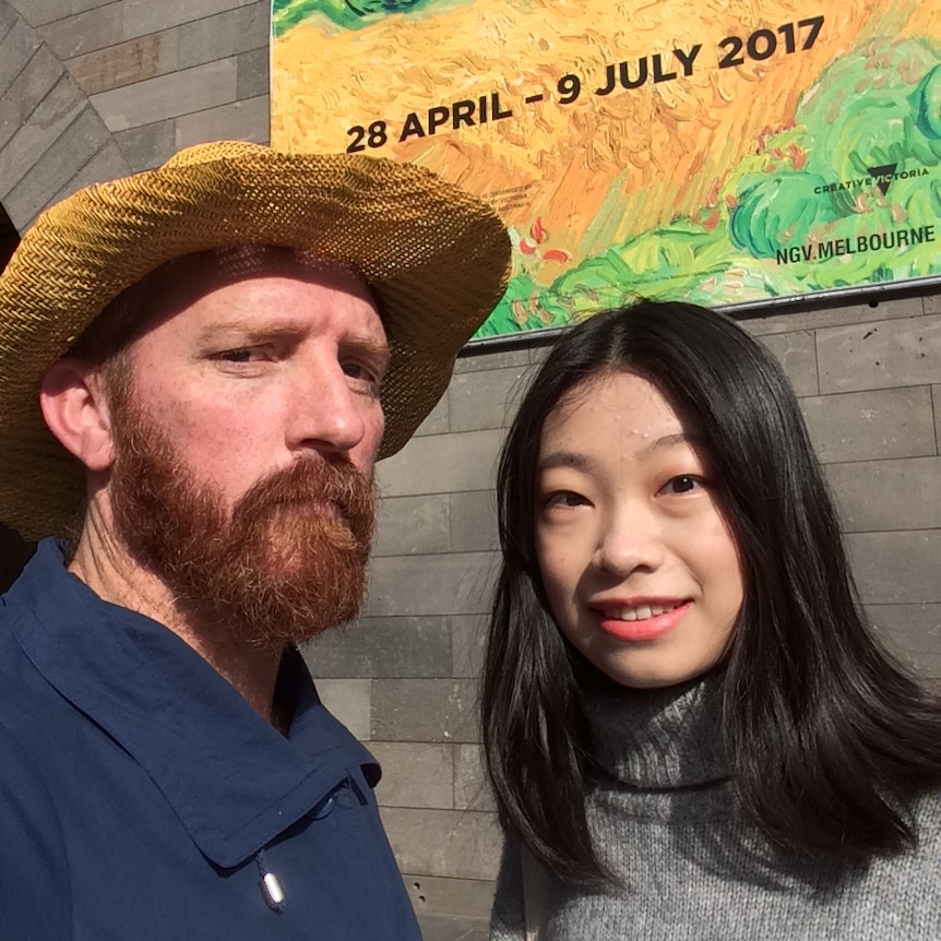 A serious-looking man with a red beard and straw had stands next to a smiling woman