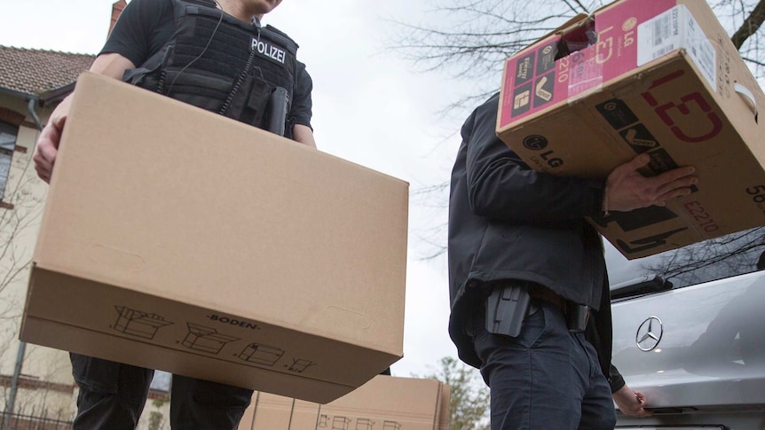 Police officers carrying boxes out of a house after an apartment raid in Berlin
