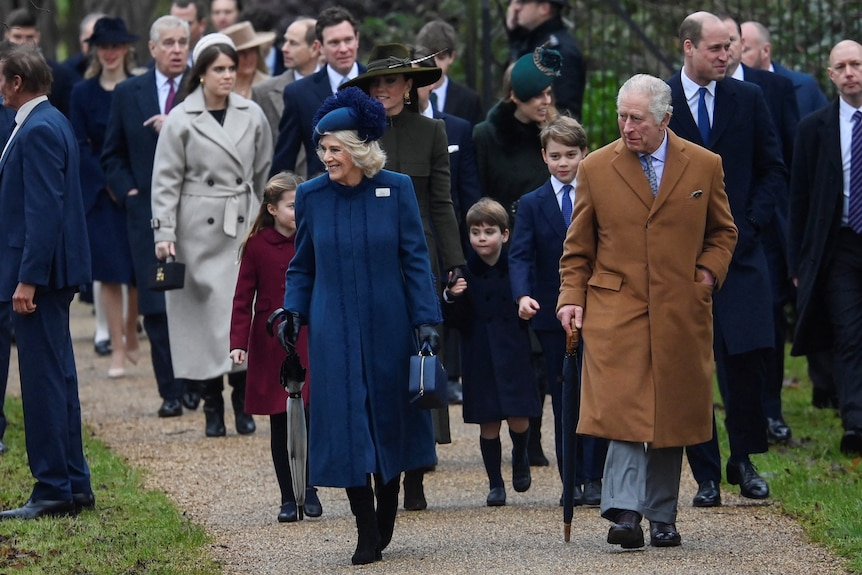Król Karol i królowa Camilla idą wiejską drogą przed innymi członkami rodziny królewskiej