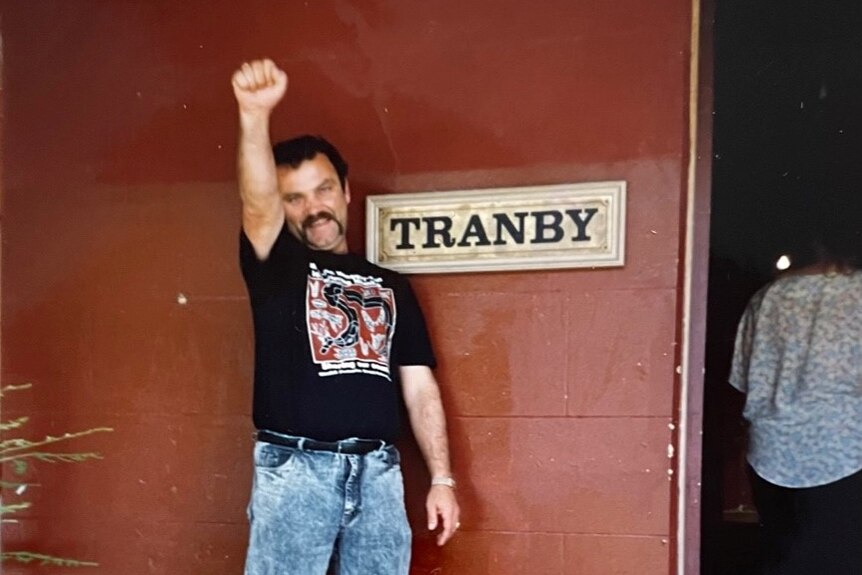 A man, standing next to a sign that says 'Tranby', holds his fist in the air