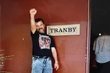 A man, standing next to a sign that says 'Tranby', holds his fist in the air