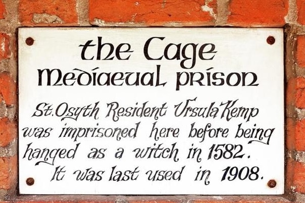 A plaque against brick reads: The Cgae, medieval prison. Ursula Kemp was imprisoned here before being hanged as a witch in 1582