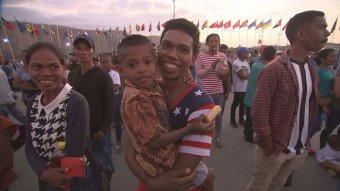 A smiling man holds a small boy in a crowd of people surrounded by flag poles