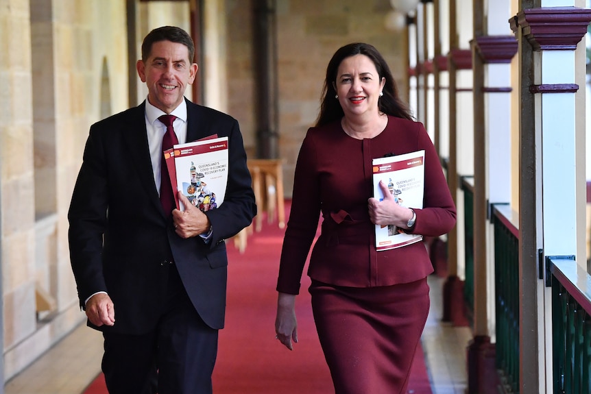 Cameron Dick and Annastacia Palaszczuk walk through parliament house holding the budget.