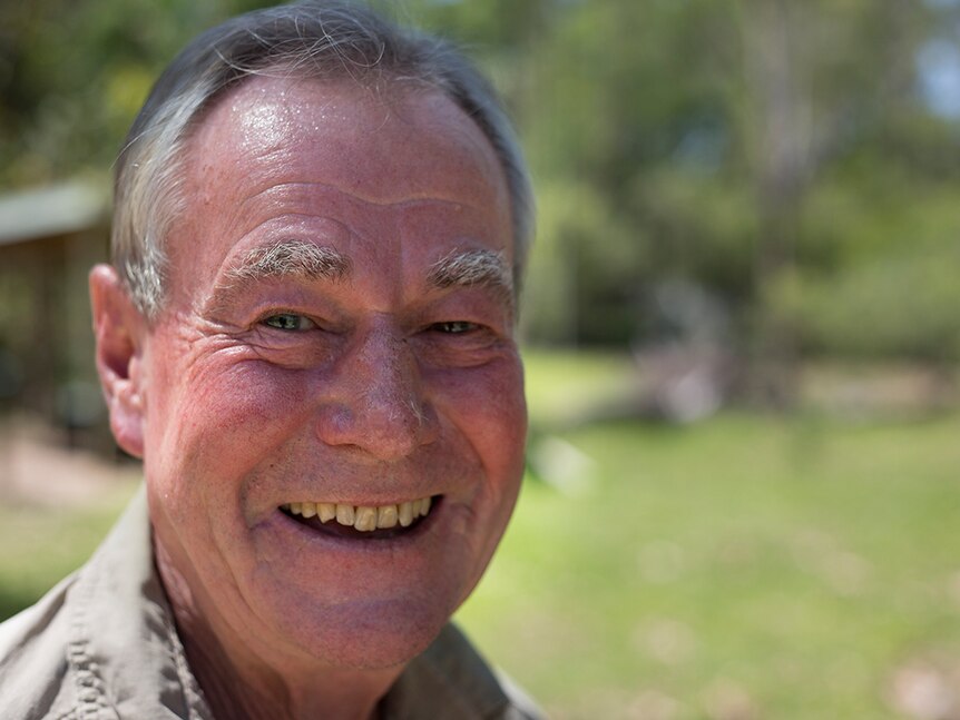 A close up of a man aged in his 60s smiling at the camera. Background blurred.