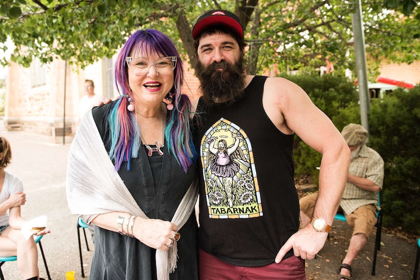 Heather Croall and Antoine Carabinier stand under a tree smiling.