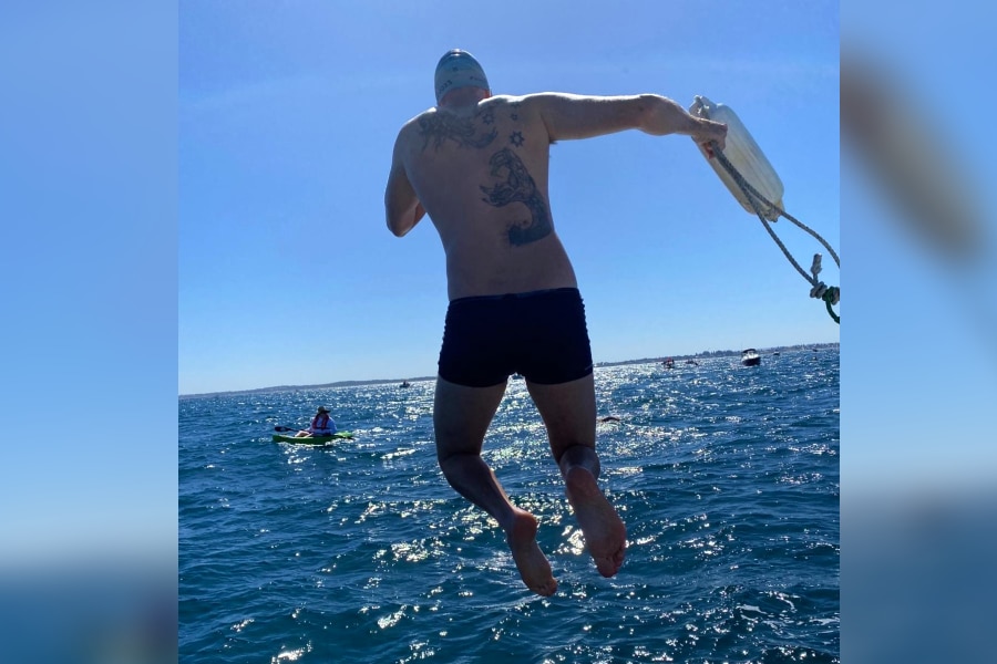 Um nadador salta de um barco usando boné e sunga