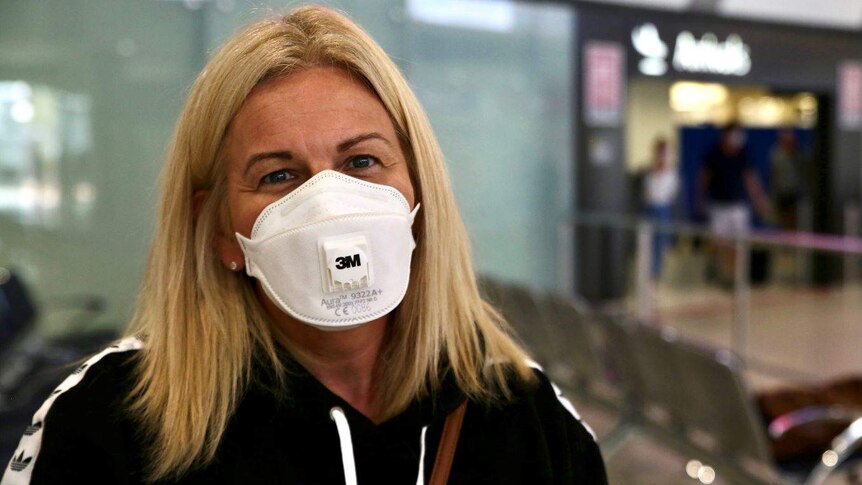 A woman smiles while wearing a face mask in a public area of an airport.