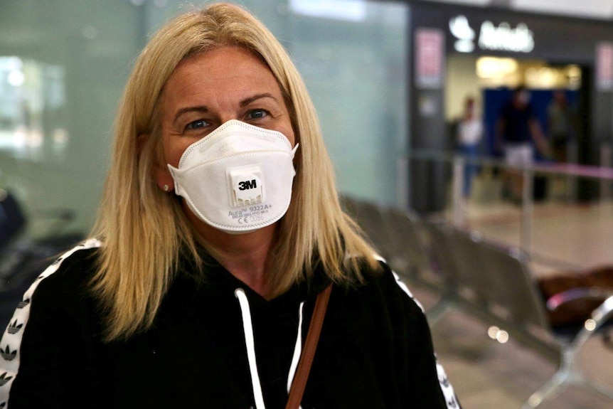 A woman smiles while wearing a face mask in a public area of an airport.