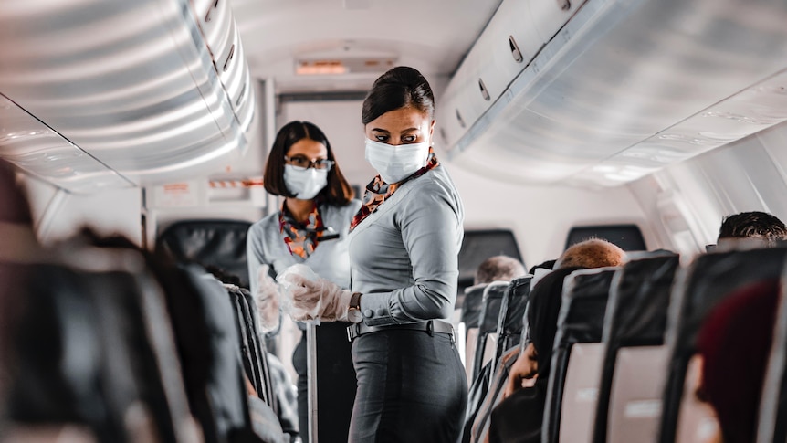 two flight attendants wear masks while serving drinks