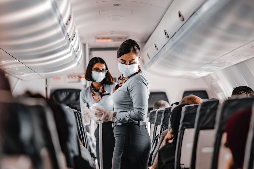 two flight attendants wear masks while serving drinks