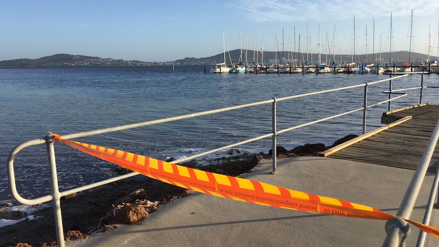Orange tape cordons off a jetty at Princess Royal Sailing Club in Albany, with yachts moored in the background.
