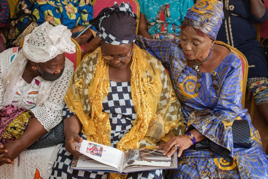 Three women in Guniea sit together looking at a book. 
