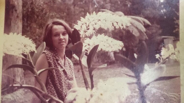 An old photo of a woman standing under a blossoming orchid.