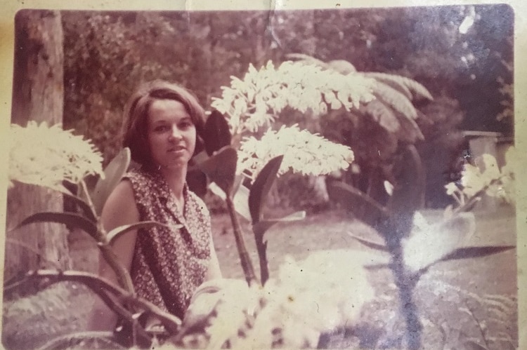 An old photo of a woman standing under a blossoming orchid.