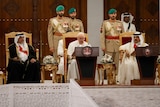 Pope Francis sits between Bahrain's king and prince in gold chairs with military officials behind. 