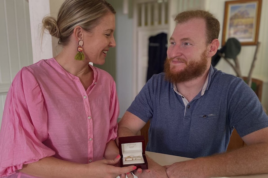 A man and a woman look into each other's eye as they hold a wedding ring