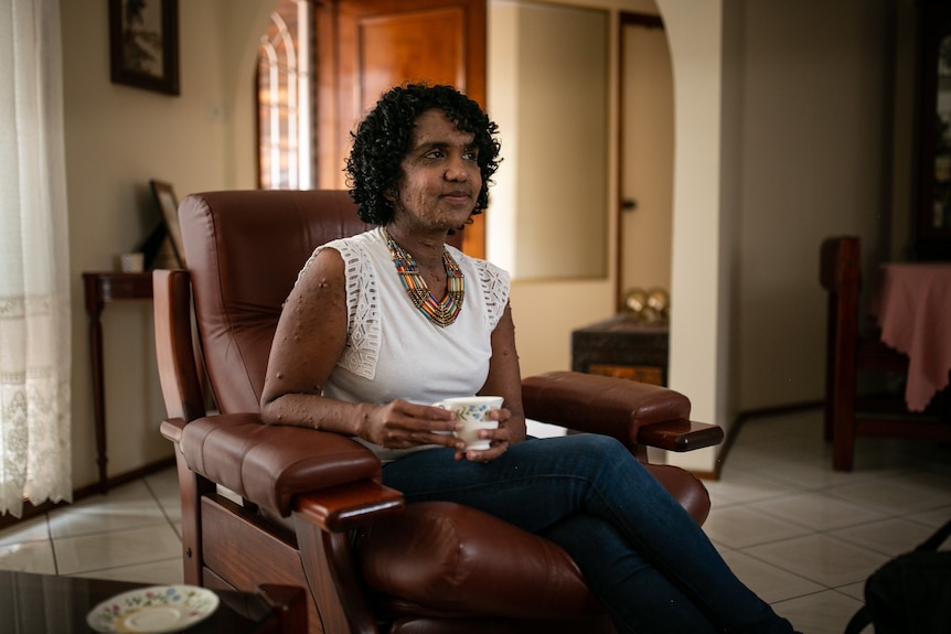 A woman sits on a chair while holding a tea