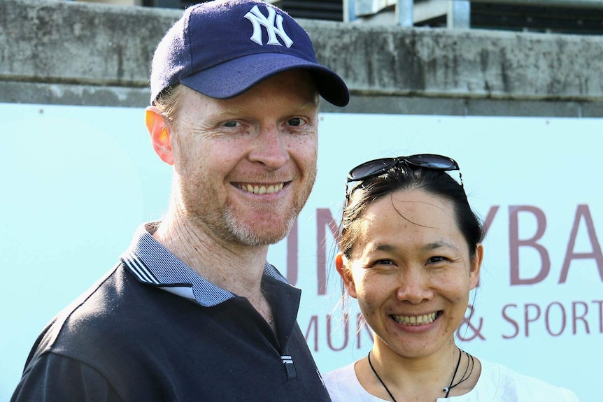 A couple standing and smiling on the edge of a football oval
